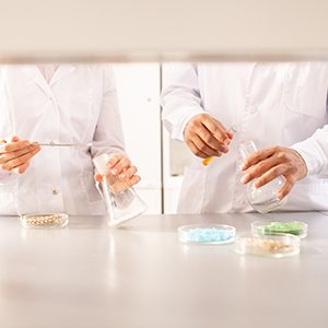 Close-up of unrecognizable agricultural scientists in lab coats standing at lab bench and making experiments with plants