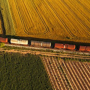 Rail freight transport, aerial view of train passing on railway through cultivated fields in countryside