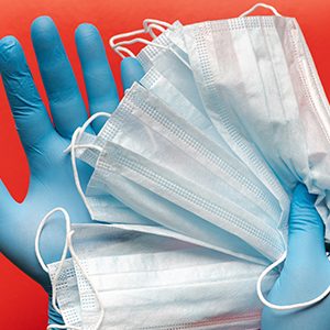 Doctor holds respiratory surgical face mask in hands blue medical gloves on red background. Pandemic corona virus, insurance, airborne diseases, SARS, grippe. Medical masks for human cover nose, mouth