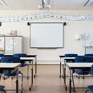 School desk and chairs in empty modern classroom. Empty class room with white board and projector in elementary school. Primary classroom with smartboard and alphabet on wall.