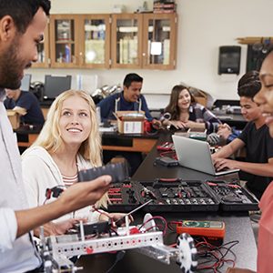 Teacher With Female Pupils Building Robotic Vehicle In Science Lesson