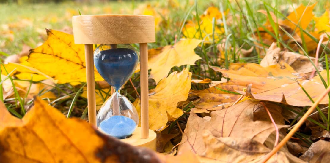 Sand hourglass and autumn leaves representing permanent daylight time in Alberta