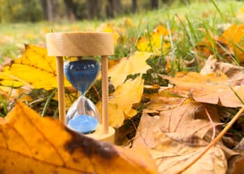 Sand hourglass and autumn leaves representing permanent daylight time in Alberta